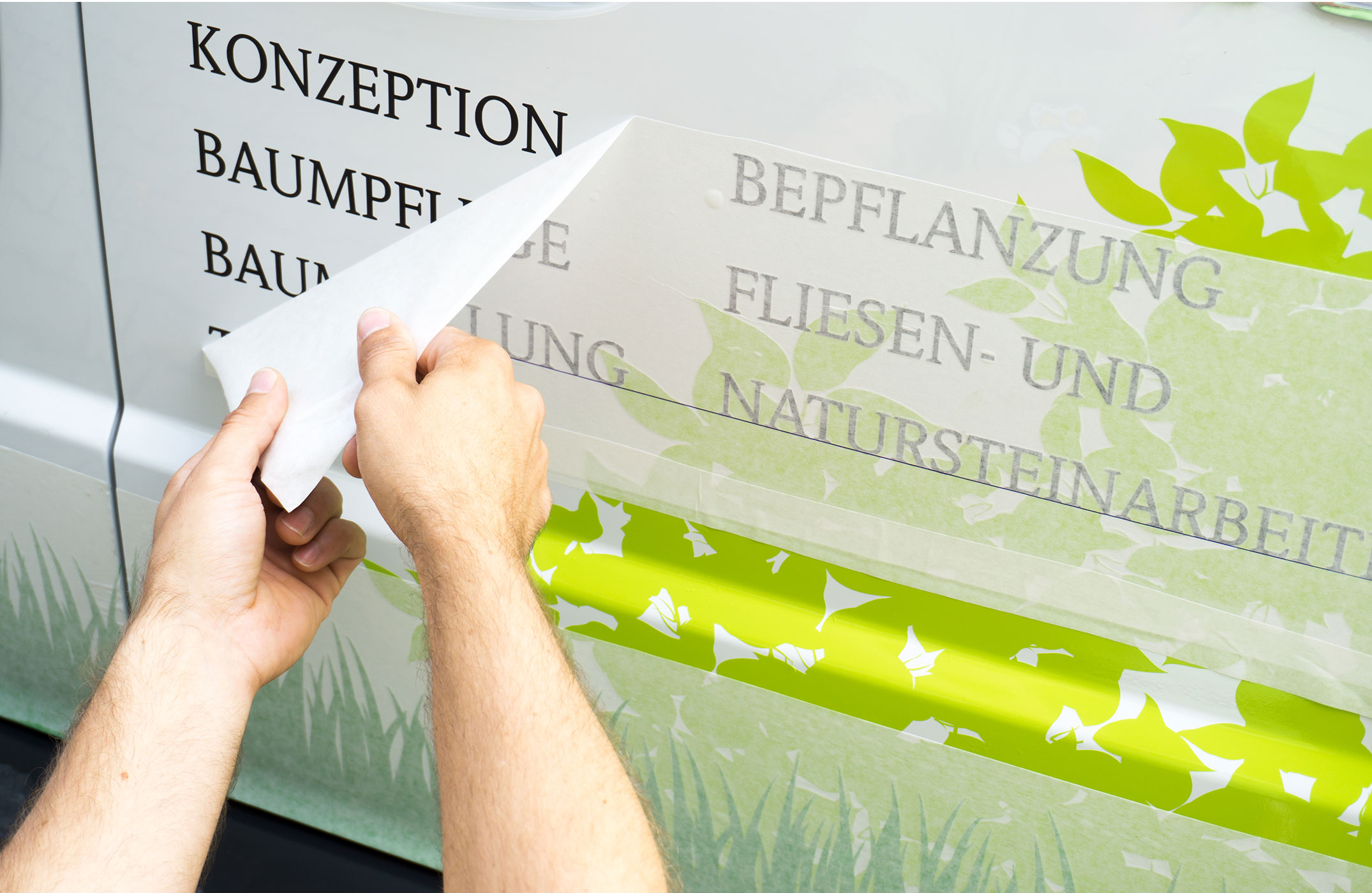 Mann verklebt Folienschriftzüge auf einem Fahrzeug